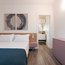 Modernes Schlafzimmer mit Doppelbett, abstrakter Kunst und Blick ins Badezimmer